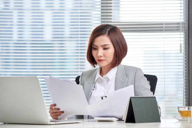 Glückliche asiatische Frau, die im Büro arbeitet. Frau, die einige Papierkram am Arbeitsplatz durchläuft.