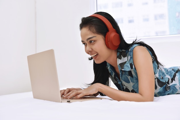 Glückliche asiatische Frau, die Laptop verwendet und die Musik genießt