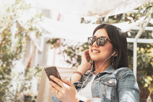 Glückliche asiatische Frau, die Telefon für das Hören eine Musik verwendet.