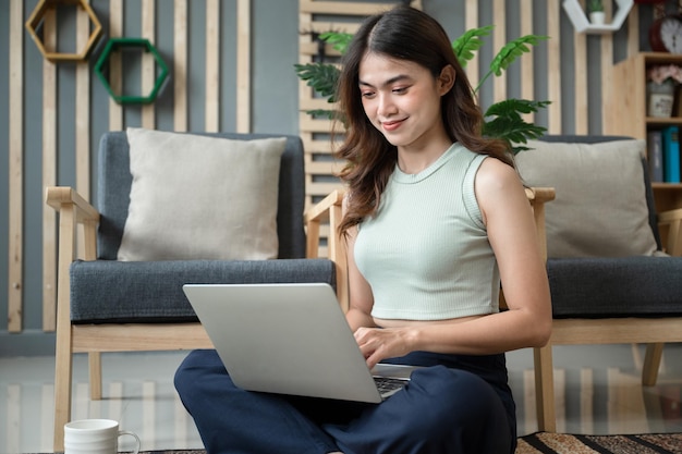 Foto glückliche asiatische frau, die zu hause mit notebook-computer im wohnzimmer aufwacht