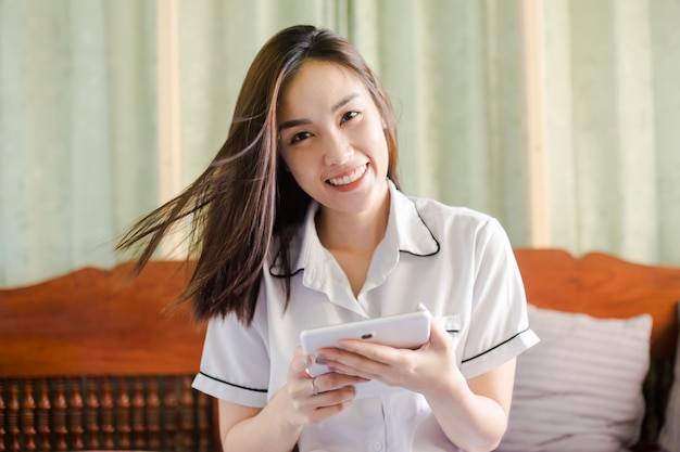 Glückliche asiatische Frau halten Smartphone und lächeln im Schlafzimmer