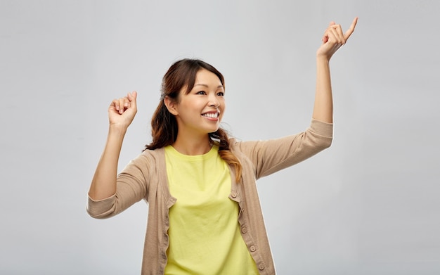 glückliche asiatische Frau tanzt über einem grauen Hintergrund