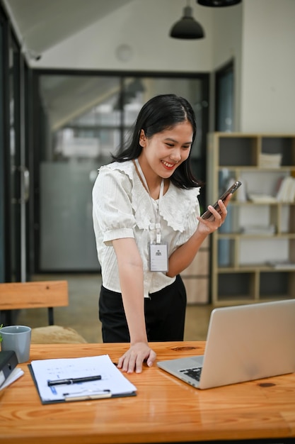 Glückliche asiatische Geschäftsfrau beugt sich über den Tisch und schaut auf den Bildschirm ihres Laptops