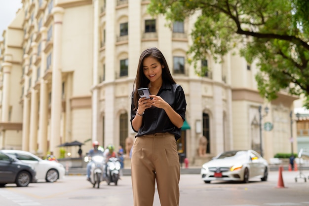 Glückliche asiatische Geschäftsfrau im Freien in der Stadtstraße mit Handy beim SMSen