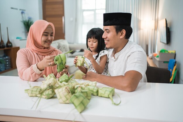 Glückliche asiatische muslimische Familie, die zusammen zu Hause vor eid mubarak Ketupat macht