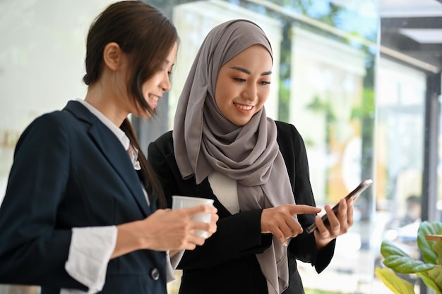 Glückliche asiatische muslimische Geschäftsfrau, die während der Mittagspause mit ihrer Kollegin plaudert