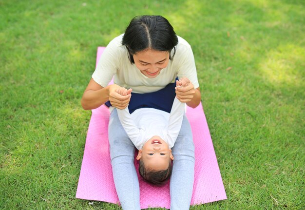 Glückliche asiatische Mutter, die mit ihrem Sohn spielt und auf grünem Rasen am Park liegt.