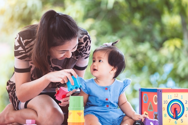 Glückliche asiatische Mutter und nettes kleines Baby, die zusammen mit dem Spielzeug spielt