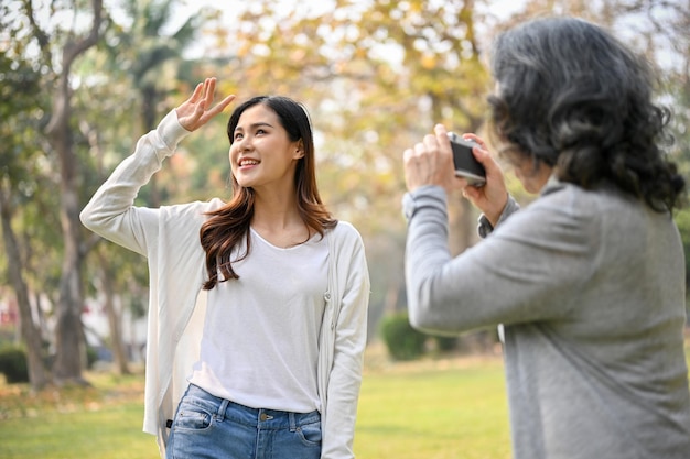 Glückliche asiatische Oma, die ein Foto ihrer Enkelin macht, während sie im Park spazieren geht