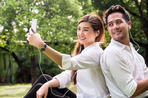 Glückliche asiatische Paare, die ein selfie mit intelligenter Telefonkamera im Park nehmen