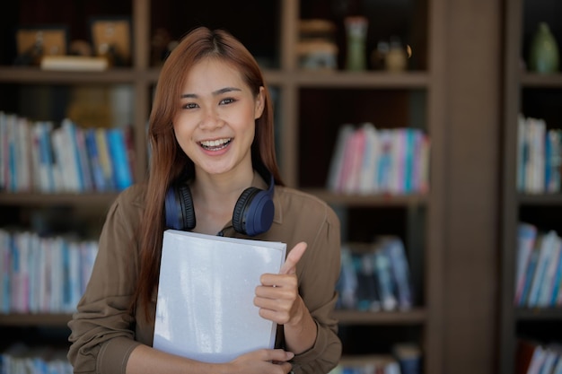 Glückliche asiatische Studentin mit Daumen nach oben in der Bibliothek