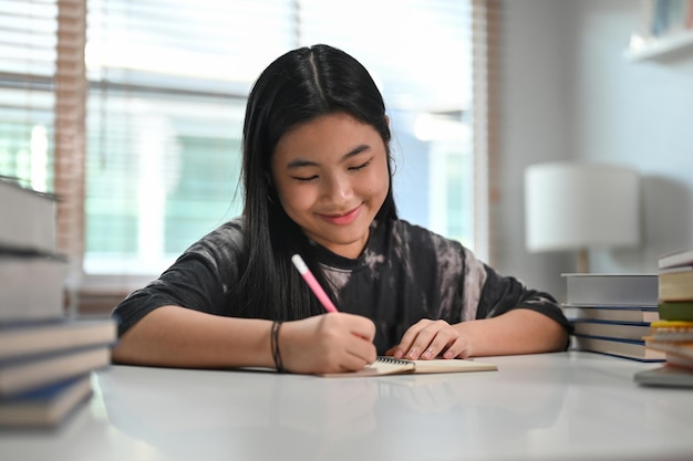 Glückliche asiatische Teenagerin, die zu Hause Hausaufgaben macht