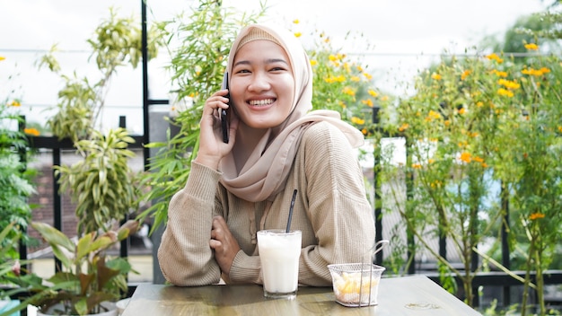 Glückliche Asien-Hijab-Frau, die Smartphone benutzt und anruft, im Café sitzt