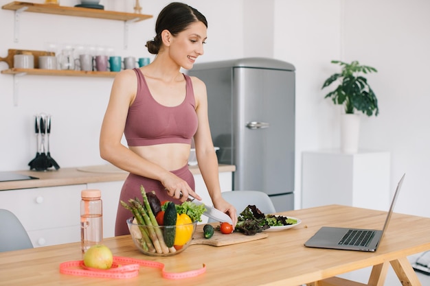 Glückliche athletische Bloggerin bereitet einen Salat mit frischem Gemüse zu