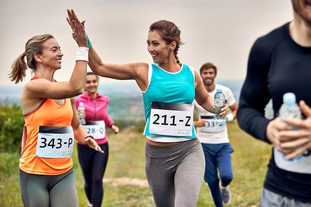 Glückliche athletische Frauen, die einen Marathon laufen und sich während des Rennens in der Natur Highfives geben
