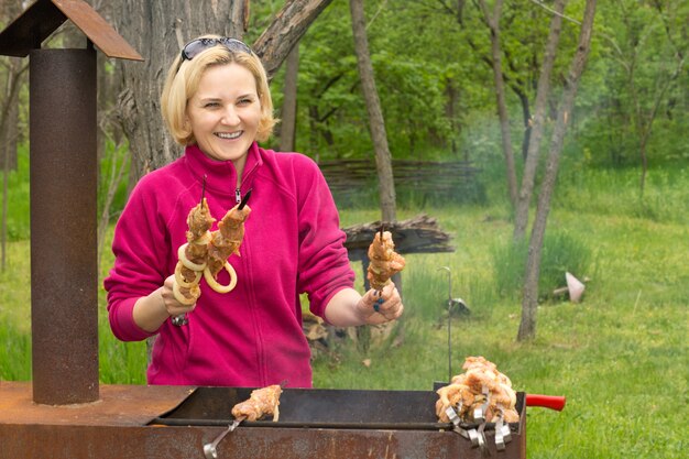 Glückliche attraktive blonde Frau, die auf einem BBQ kocht