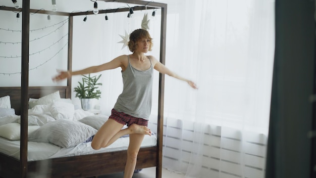 Glückliche attraktive Frau, die zu Hause Yoga-Übungen in der Nähe des Bettes im Schlafzimmer macht