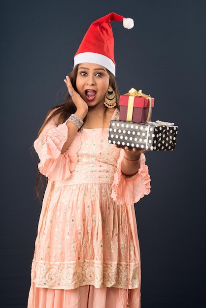 Glückliche aufgeregte junge Frau in einem Weihnachtsmann-Hut mit Geschenkboxen über grauem Hintergrund Weihnachtskonzept