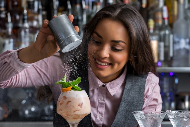 Glückliche Barkeeperin, die dem Cocktail Puderzucker hinzufügt