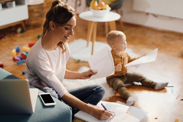 Glückliche berufstätige Mutter, die sich Notizen macht, während sie zu Hause den Papierkram durchgeht