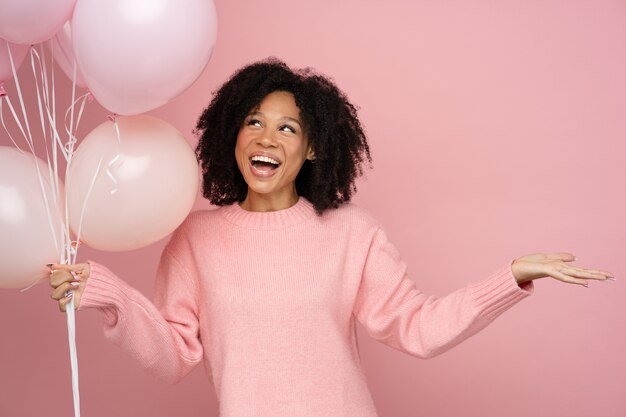 Glückliche biracial Frau mit dem lockigen Haar, das viele Luftballons hält