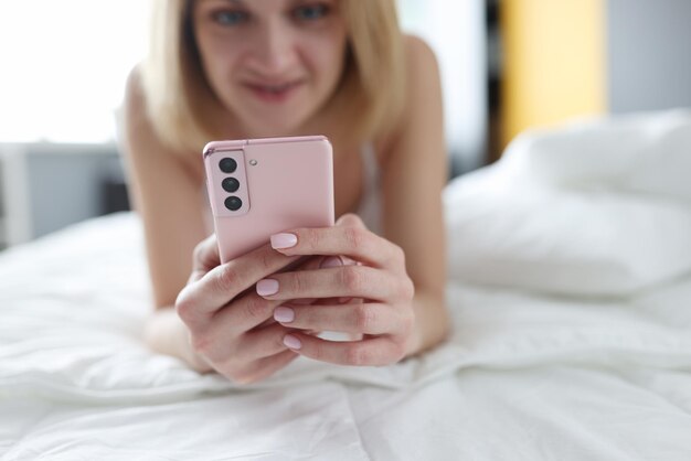 Glückliche blonde Frau liegt mit einem Smartphone auf dem Bett