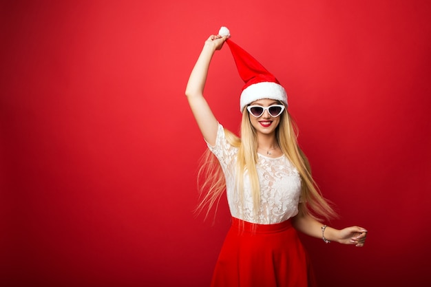 Glückliche blondine in sankt-hut auf rotem lokalisiertem hintergrund. sonnenbrille mit weißem rand.