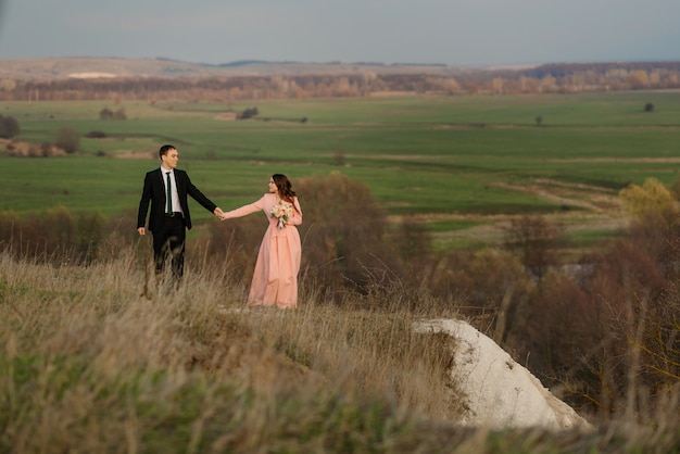 Glückliche Braut und Bräutigam an ihrem Hochzeitstag. Bräutigam und Braut gehen auf einer hügeligen Gegend mit einer schönen Aussicht.