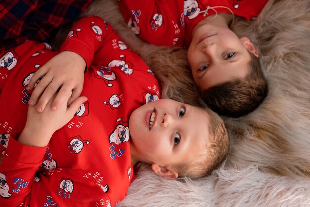 Glückliche Brüder im Pyjama liegen auf dem Teppich am Weihnachtsbaum und haben Spaß mit der Freude an der Weihnachtskaukasierin ...