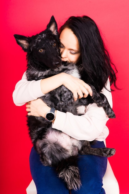 Glückliche brünette Dame in Gelegenheitsbekleidung umarmt Mudi Haustier Hund Studio Hintergrund