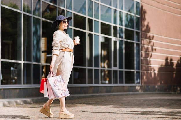 Glückliche Brunettefrau, die draußen Einkaufstaschen hält. Shopoholic-Frau, die mit den Einkäufen zufrieden ist