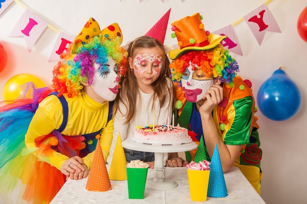 Glückliche Clowns blasen die Kerzen auf der Geburtstagstorte im Urlaub aus