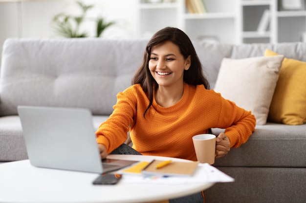 Glückliche Dame aus dem Osten, die von zu Hause aus mit einem Laptop arbeitet