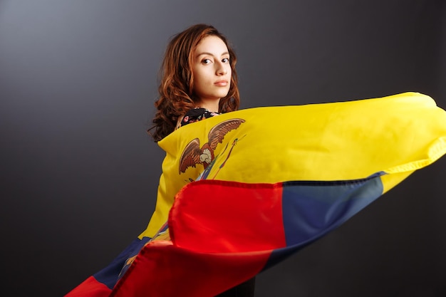 Glückliche ecuadorianische Frau, die mit einer Flagge lächelt und posiert, die über einem grauen Hintergrund isoliert ist