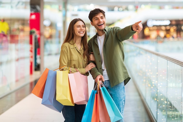 Glückliche Ehepartner, die Einkaufstüten halten und mit dem Finger auf den Einkauf im Hypermarkt zeigen