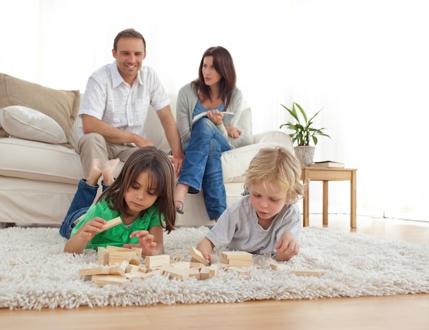 Glückliche Eltern auf dem Sofa, das ihre Kinder spielen auf dem Boden betrachtet