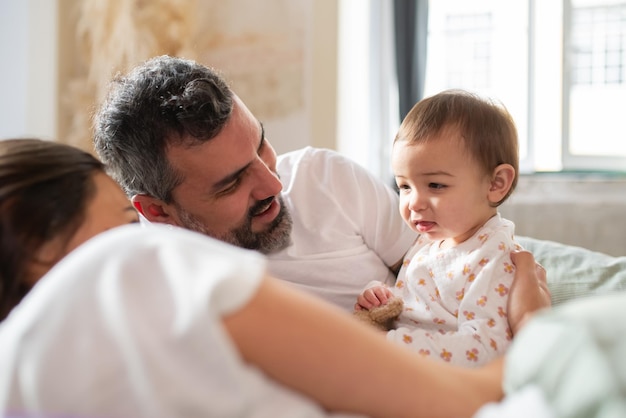 Glückliche Eltern, die im Bett liegen und morgens den kleinen Sohn betrachten. Familie mit kleinem Kind wacht zusammen auf. Konzept der Familie zu Hause