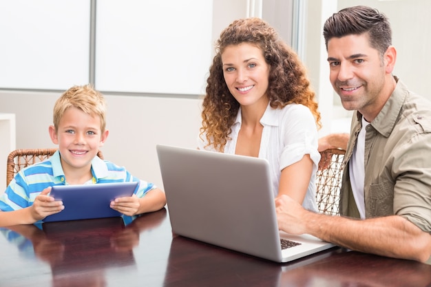 Glückliche Eltern, die mit dem Sohn verwendet Tablette und Laptop sitzen