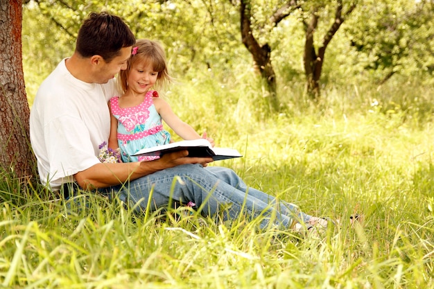 Glückliche Eltern mit einem Kind lesen die Bibel im Naturpark