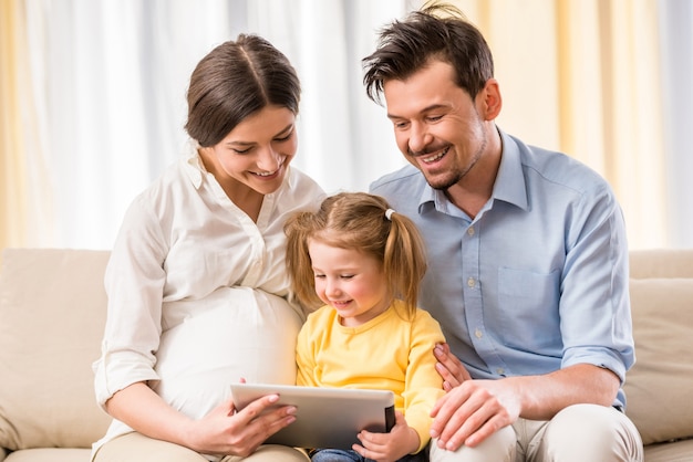 Glückliche Eltern und ihre süße Tochter verwenden Tablet.