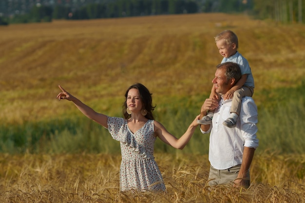 Glückliche Eltern und Kinder, die durch ein Weizenfeld gehen. Mutter, Vater und kleiner Junge verbringen zusammen im Freien. Familie auf Sommerwiese