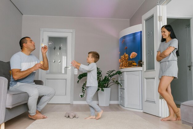 Glückliche Eltern und Töchter blasen mit ihrem Häuschen Seifenblasen im Haus