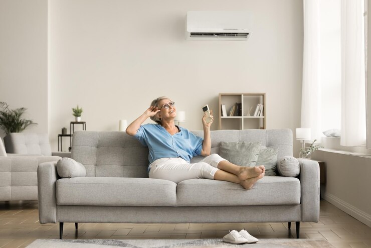 Foto glückliche, entspannte ältere dame mit ac-fernbedienung, startkonditionierung, split-system, kühlluft, ruhe auf einer weichen, stilvollen couch im modernen innenraum, genießt das behagliche klima in der wohnung