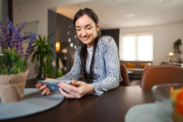 Glückliche, entspannte junge Frau, die im Wohnzimmer ein Mobiltelefon benutzt