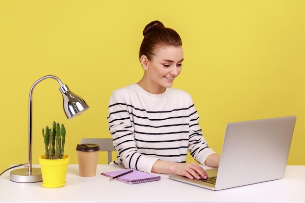 Glückliche erfolgreiche Geschäftsfrau, die am Büroarbeitsplatz sitzt und mit einem Lächeln auf dem Laptop tippt