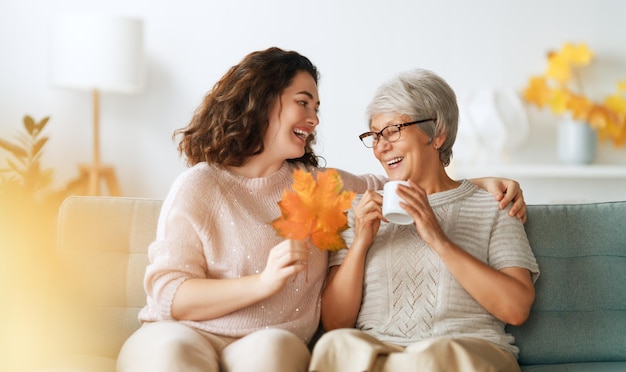 Glückliche erwachsene Frau und ihre ältere Mutter mit Herbstblättern im Haus