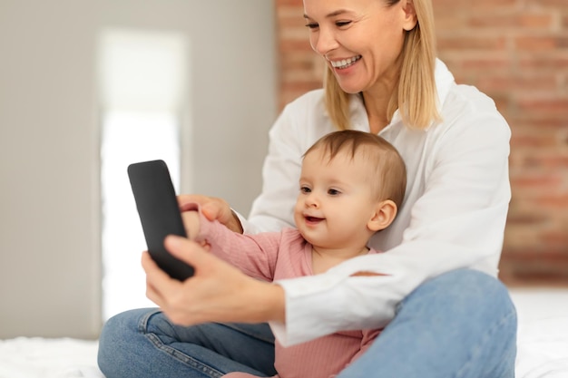 Glückliche europäische Mutter und kleines Mädchen spielen mit Mobiltelefonen pädagogische Spiele online oder