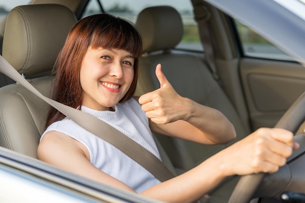 Glückliche Fahrerin lächelt und zeigt Daumen nach oben, während durch das Autofenster Blick auf eine Dame, die ihr Auto fährt, um in ihrem Urlaub zu reisen