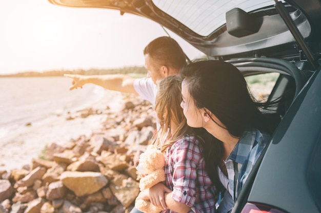 Glückliche Familie auf einem Roadtrip in ihrem Auto. Papa, Mama und Tochter sind am Meer, am Meer oder am Fluss unterwegs. Sommerfahrt mit dem Auto.