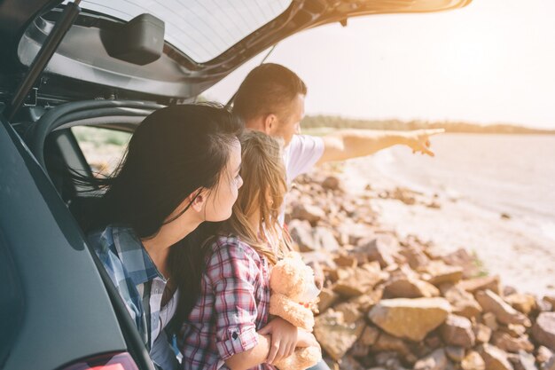 Glückliche Familie auf einem Roadtrip in ihrem Auto. Vater, Mutter und Tochter reisen am Meer, am Meer oder am Fluss. Sommerfahrt mit dem Auto